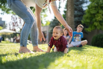 女人穿着白色衬衫和蓝色牛仔裤帮助婴儿绿色草地上爬
